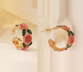 A pair of gold-colored French style floral hoops earrings with pink and green details, displayed against a white background.